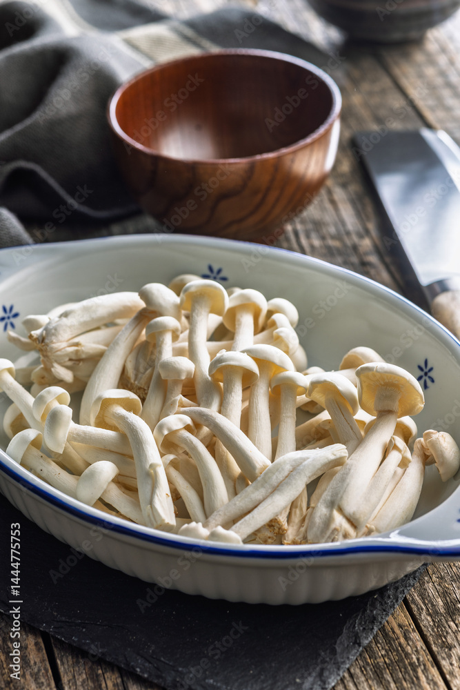 Raw white shimeji mushrooms in bowl on cutting board.