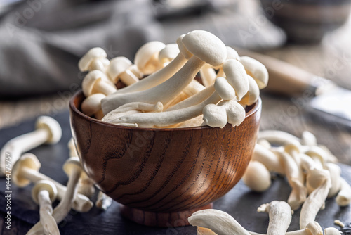 Raw white shimeji mushrooms in bowl on cutting board.