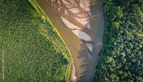 Aerial view of a river separating lush green farmland and dense forest.