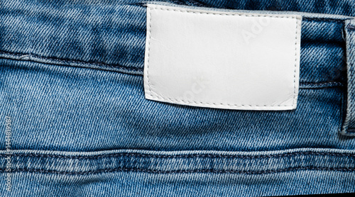 Close-up View of Denim Jeans Featuring Blank White Label on the Waistband. The Fabric Reveals Texture and Stitching, Emphasizing Quality Construction.