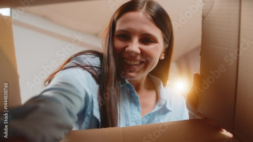 Happy woman unpacking delivery parcel at home. Smiling satisfied young girl shopper online shop customer opening cardboard box receiving purchase gift by fast postal shipping. View inside from the box