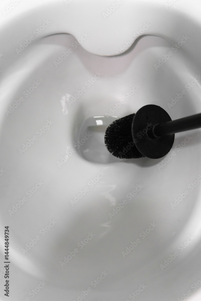 Using a black toilet brush for scrubbing the interior of a white toilet bowl, promoting cleanliness and hygiene in the bathroom while effectively combating germs and bacteria. Vertical photo