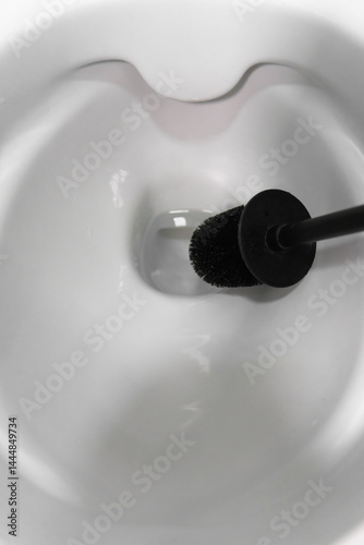 Obraz na płótnie Using a black toilet brush for scrubbing the interior of a white toilet bowl, promoting cleanliness and hygiene in the bathroom while effectively combating germs and bacteria. Vertical photo w salonie