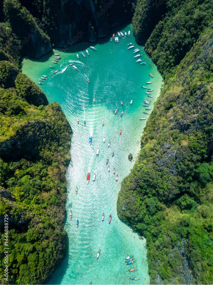Vertical drone view of a narrow tropical bay at Ko Phi Phi with longtail boats and vibrant turquoise waters, ideal for exotic travel ads, Southeast Asia vacation and adventure lifestyle visuals.