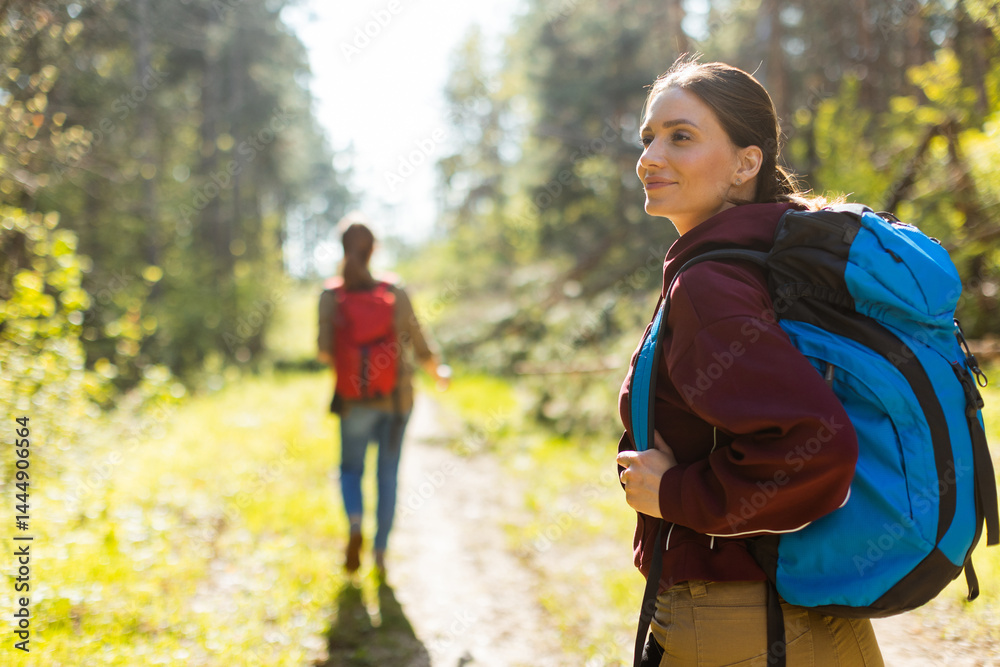 Exciting adventure awaits as two friends explore a sunlit forest trail with vibrant backpacks on a beautiful day