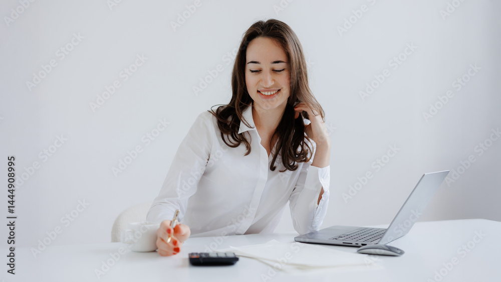 Young woman engaged in work at a bright desk while using a laptop and writing notes in a modern office setting