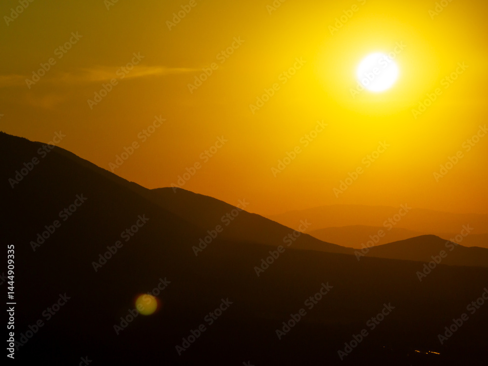 Obraz premium Summer sunset over Pirin Mountains silhouette, Bulgaria, captured from aerial perspective, showcasing layered ridge silhouettes, golden hues, and calm alpine wilderness. Orange sun disk