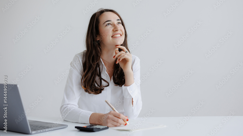 Young woman brainstorming ideas at a desk with laptop and calculator in a bright office space