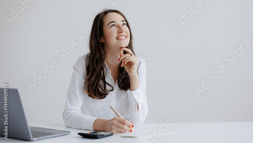 Obraz na płótnie Young woman brainstorming ideas at a desk with laptop and calculator in a bright office space w salonie