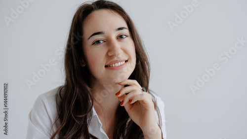 Smiling young woman with long hair in a simple white shirt poses confidently in a bright room