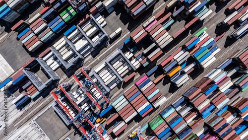 Aerial top view of organized stacks of colorful shipping containers at a busy cargo yard. The image reflects the logistics efficiency and volume of global trade through maritime transport.