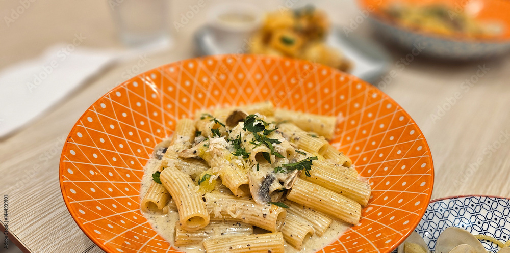 Mushroom penne pasta with cream truffle sauce serving on bright orange plate