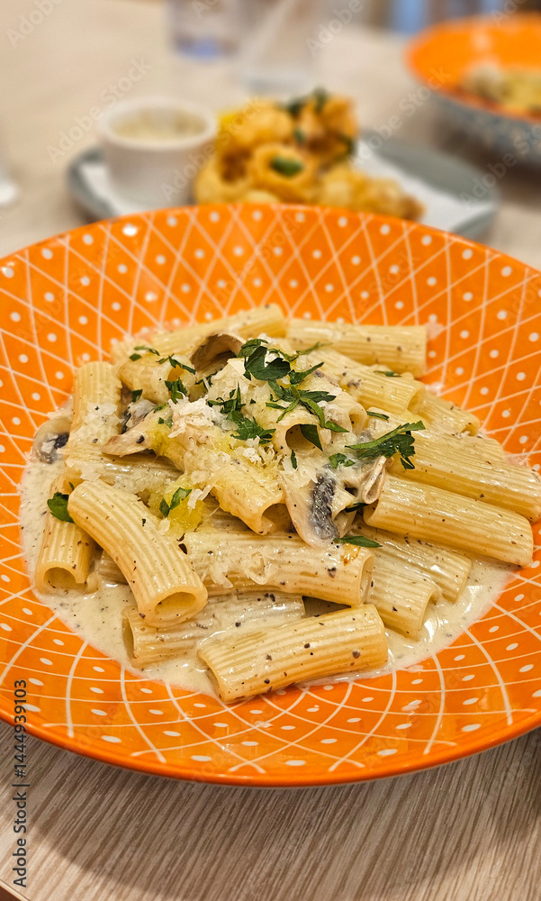 Mushroom penne pasta with cream truffle sauce serving on bright orange plate