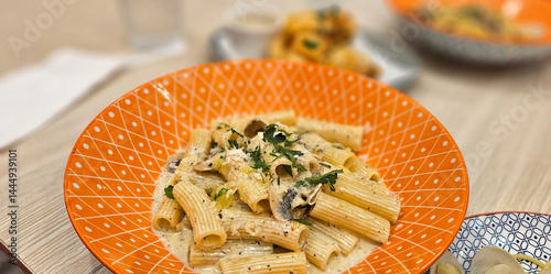 Mushroom penne pasta with cream truffle sauce serving on bright orange plate