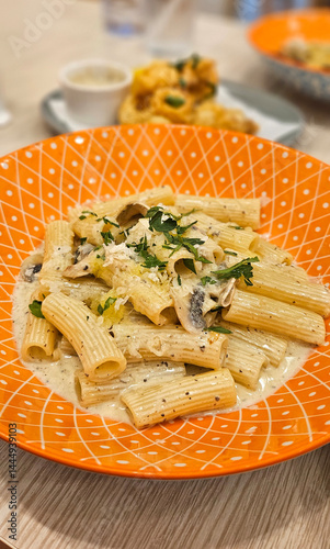 Obraz na płótnie Mushroom penne pasta with cream truffle sauce serving on bright orange plate w salonie