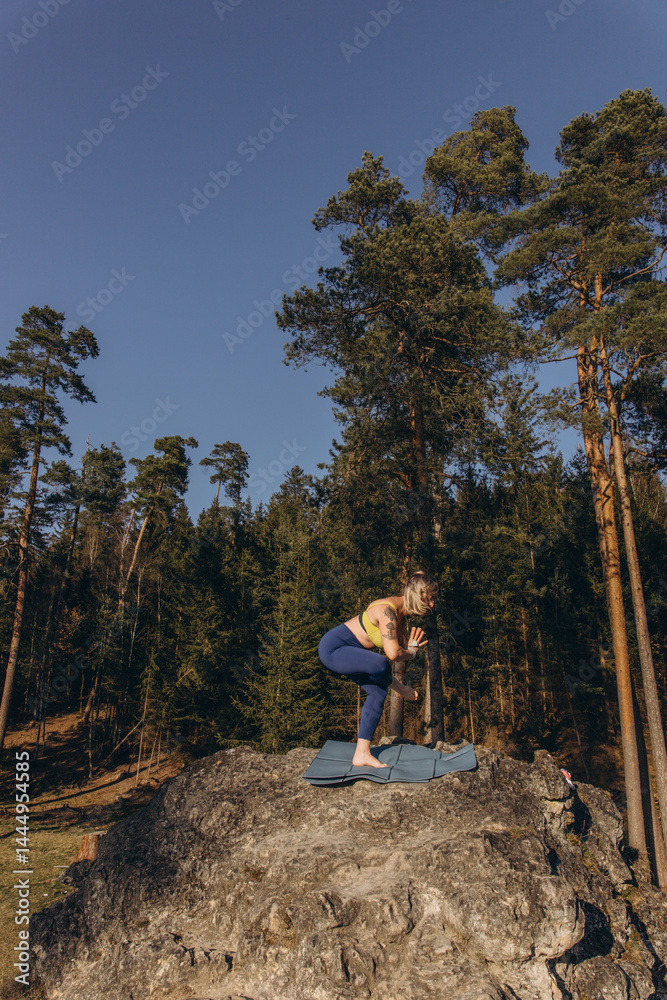 Fototapeta premium A woman meditating and practicing yoga on top of a rock at sunset, embracing wellness, mindfulness, and eco-friendly living