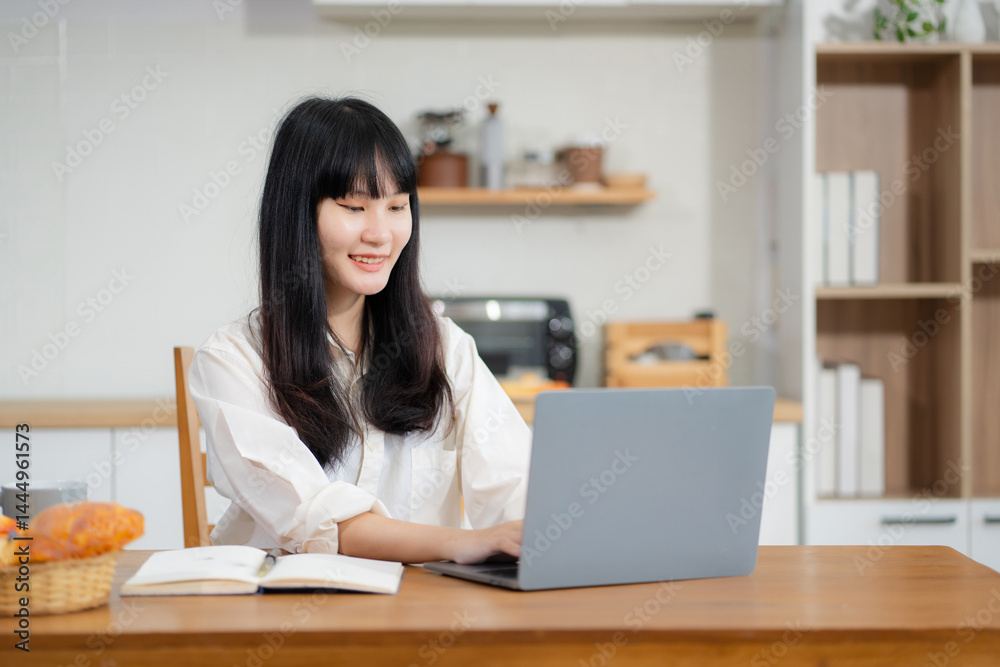 Lifestyle people, using computer working online, doing searching, sitting in the kitchen. Happy woman, entrepreneur, small business owner working online at home office.