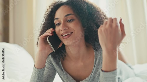 Wallpaper Mural Charming African American woman holding phone to ear while chatting during call. Twirling hair playfully with other hand and enjoying light conversation while relaxing indoors in casual gray outfit. Torontodigital.ca