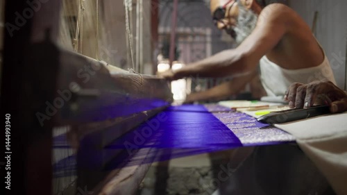 Skilled Indian artisan handweaving a Banarasi silk saree on a traditional wooden handloom. The weft shuttle moves across the fabric, creating intricate woven patterns.