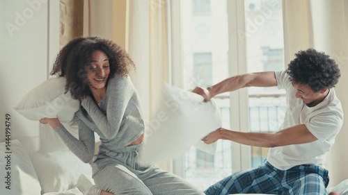 Wallpaper Mural Playful African American couple laughing and hitting each other with pillows while sitting on bed. Enjoying spontaneous pillow fight in bright room wearing casual comfy loungewear on relaxed morning. Torontodigital.ca