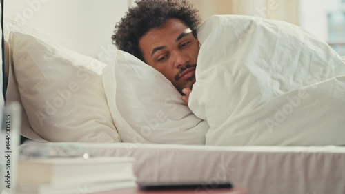 Wallpaper Mural Sleepy African American male just waking up while lying under blanket in bed. Picking up smartphone with tired eyes, checking notifications early in the morning. Starting day passively. Torontodigital.ca
