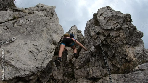 Stepping over mossy stones, a hiker follows steel cables into a narrow gorge, echoing with distant mountain breezes on Cresta Giumenta.