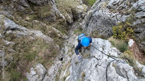 A woman steadies herself on a slippery ledge as gusts of wind buffet the exposed ridgeline of Ferrata Centenario’s via ferrata.
