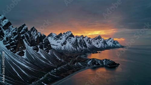 Sunset coastline with snow-dusted mountains and winding road by calm water
