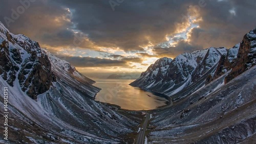 Sunset-lit winding road along snow-dusted mountains by tranquil waters
