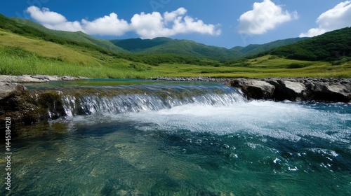 Crystal-clear mountain stream cascading over rocks. Lush green valley and hills backdrop