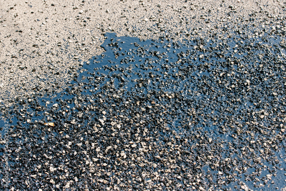 Asphalt patch closeup. Fresh asphalt patch with bitumen and resin coat applied to cracked road surface during street repair and maintenance works ensuring improved urban infrastructure quality