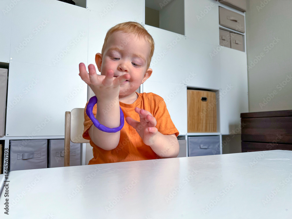A cute little red-haired boy was making a round bracelet out of blue plasticine. Early development of fine motor skills, creativity