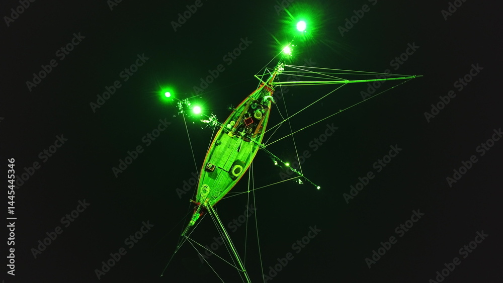 Low angle night view of a squid fishing boat using green lights to attract its prey, creating a surreal atmosphere in the darkness off the coast of Koh Phangan, Thailand