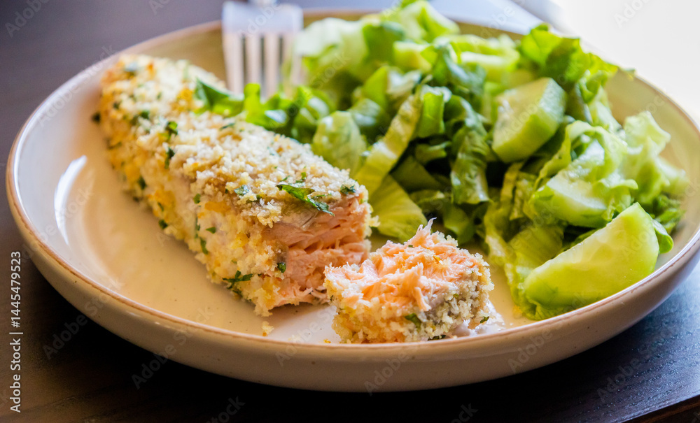 Close-up of a baked breaded salmon fillet served with a simple green salad in a dish. The salmon has a golden, crispy crust and is paired with fresh greens Close-up of a baked breaded salmon fillet served with a simple green salad in a dish. The salmon has a golden, crispy crust and is paired with fresh greens