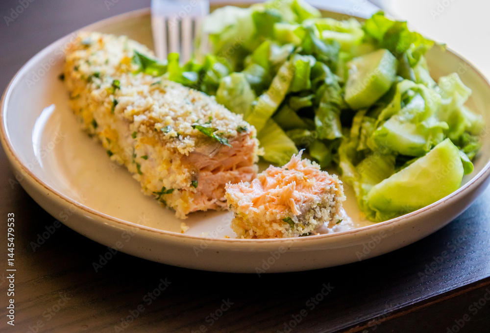 Close-up of a baked breaded salmon fillet served with a simple green salad in a dish. The salmon has a golden, crispy crust and is paired with fresh greens Close-up of a baked breaded salmon fillet served with a simple green salad in a dish. The salmon has a golden, crispy crust and is paired with fresh greens