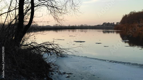 Ice floating on calm river at sunset in serene landscape. Ice chunks drift on a river as spring arrives, showcasing nature's transformation at sunset near tranquil surroundings