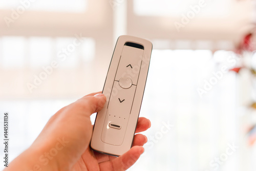 Radio remote control panel for blinds and roller shades in woman hand, white, close-up. Bright background. Blinds and curtains for smart house. Home automation, wireless technology. Electronic device.