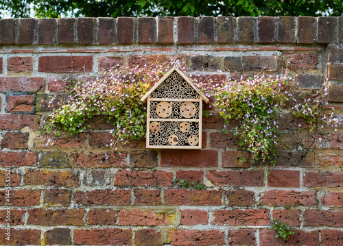 Bug house hotel for insects, surrounded by flowers, affixed to the wall at Eastcote House Gardens, in Hillingdon London UK. 