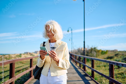 Senior woman enjoying a walk by the seaside while checking her phone