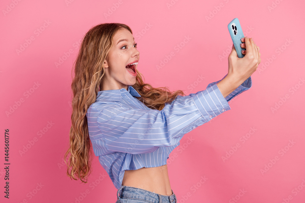 Young female student in stylish casual style taking a joyful selfie, showcasing a cheerful mood on a vibrant pink background