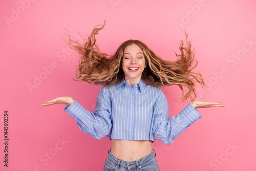Young woman with flowing wavy hair smiling joyfully in a stylish casual blue shirt against a vibrant pink background.