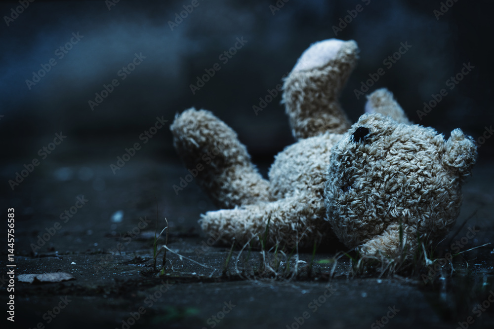 Conceptual image: lost childhood loss future, loneliness, pain and depression. Dirty toy Teddy bear lying down outdoors. Copy space.