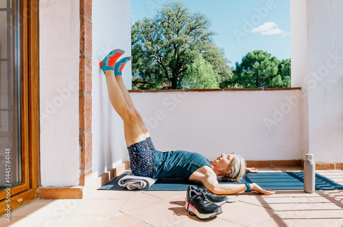 Post-run recovery: woman doing restorative yoga pose with legs up the wall on a sunny terrace
