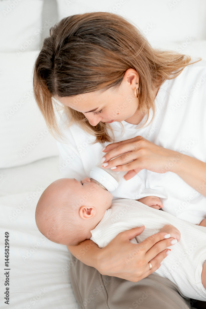 mom feeds the baby with a bottle of milk or formula, feeding the baby in her arms, a young mother feeds the newborn baby at home on the bed mom feeds the baby with a bottle of milk or formula, feeding the baby in her arms, a young mother feeds the newborn baby at home on the bed