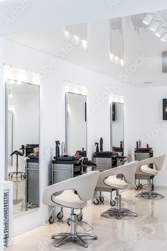 Row of modern styling chairs and mirrors in a hair salon interior, featuring professional tools and clean white walls