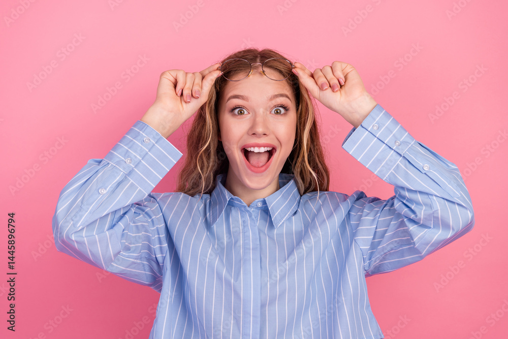 Cheerful young woman lifting glasses while expressing joyful excitement standing against a vibrant pink background Cheerful young woman lifting glasses while expressing joyful excitement standing against a vibrant pink background