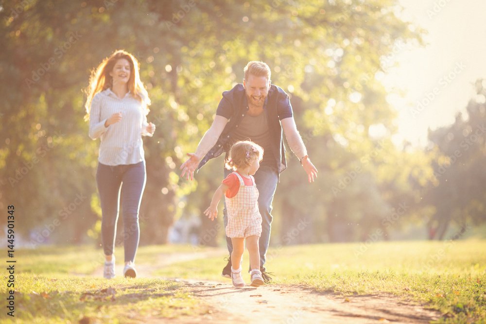 Fototapeta premium Young happy parents with their baby girl having fun outdoors