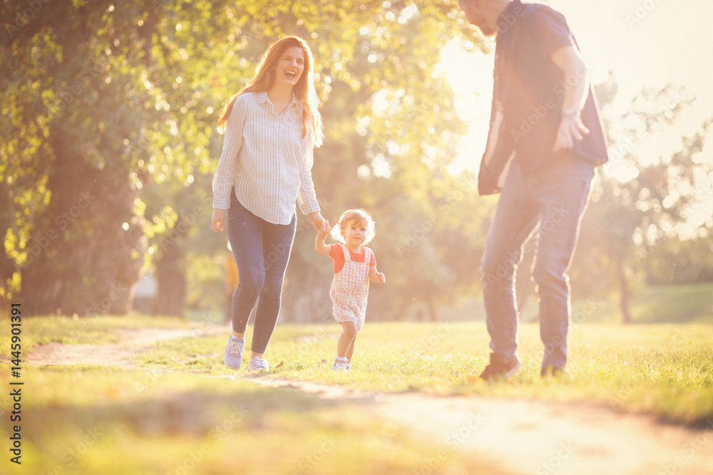 Fototapeta premium Young happy parents with their baby girl having fun outdoors