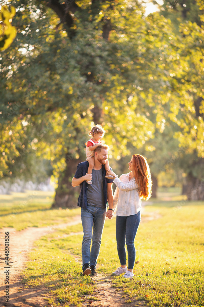 Fototapeta premium Young happy parents with their baby girl having fun outdoors