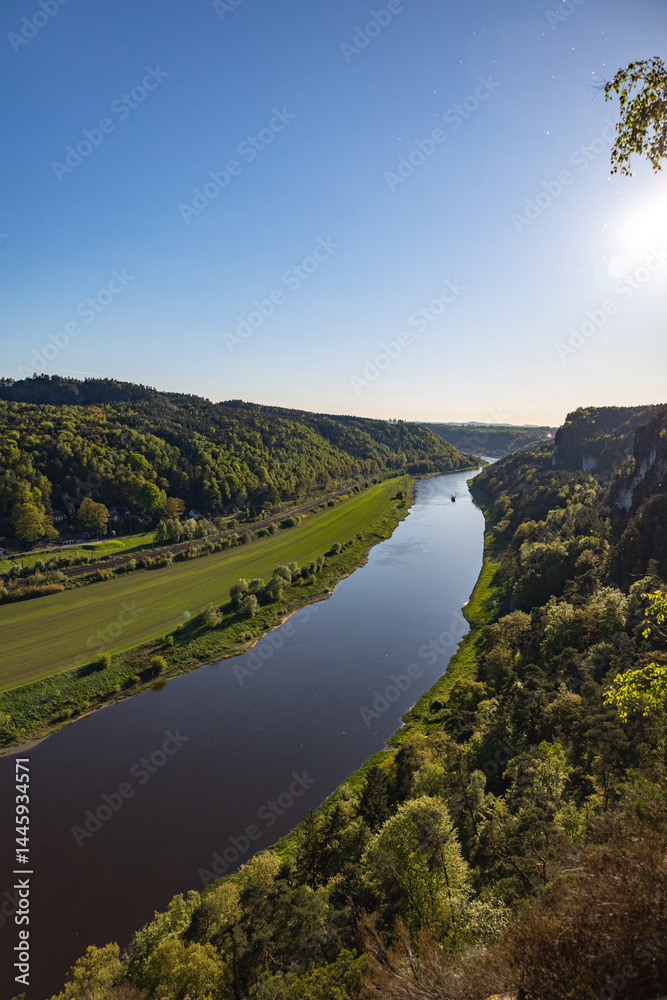 Obraz premium Scenic Sunset View Over the Elbe River Winding Through the Forested Hills of Saxon Switzerland National Park with Cliffs and Meadows